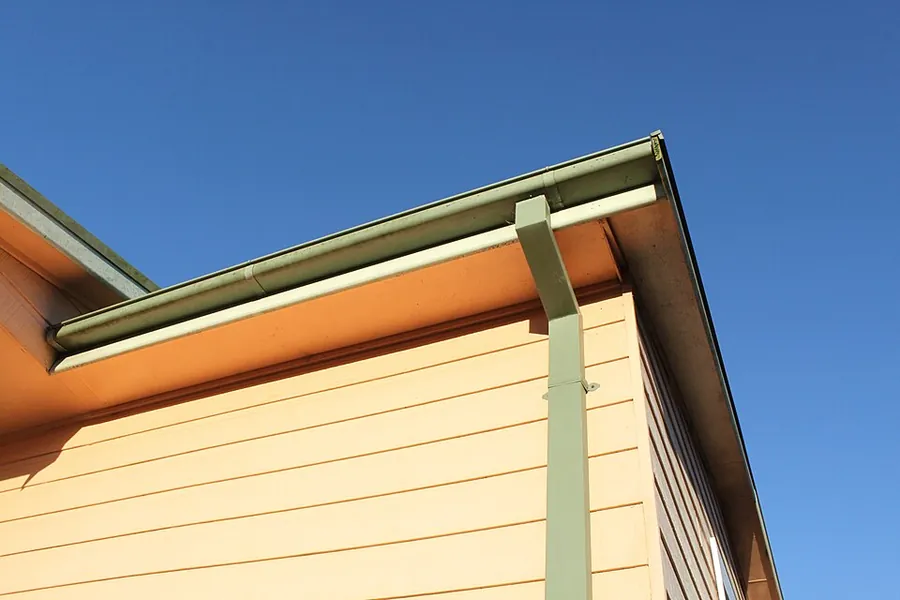 Green gutter and downspout against a yellow clapboard wall and eave