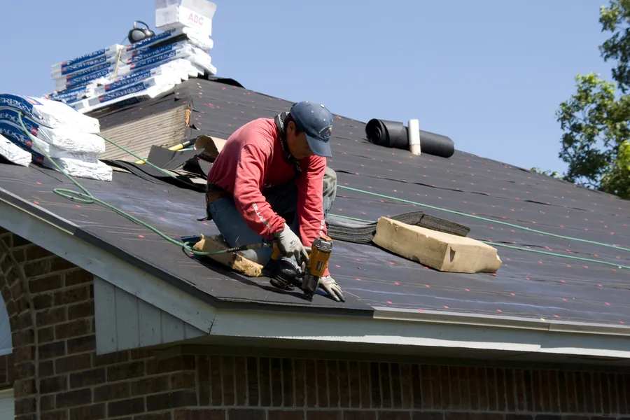A roofer nailing asphalt shingles onto a roof deck
