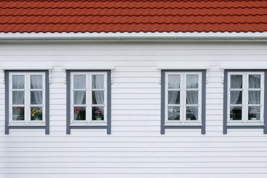 Four white-framed windows set into white lap siding below a red roof
